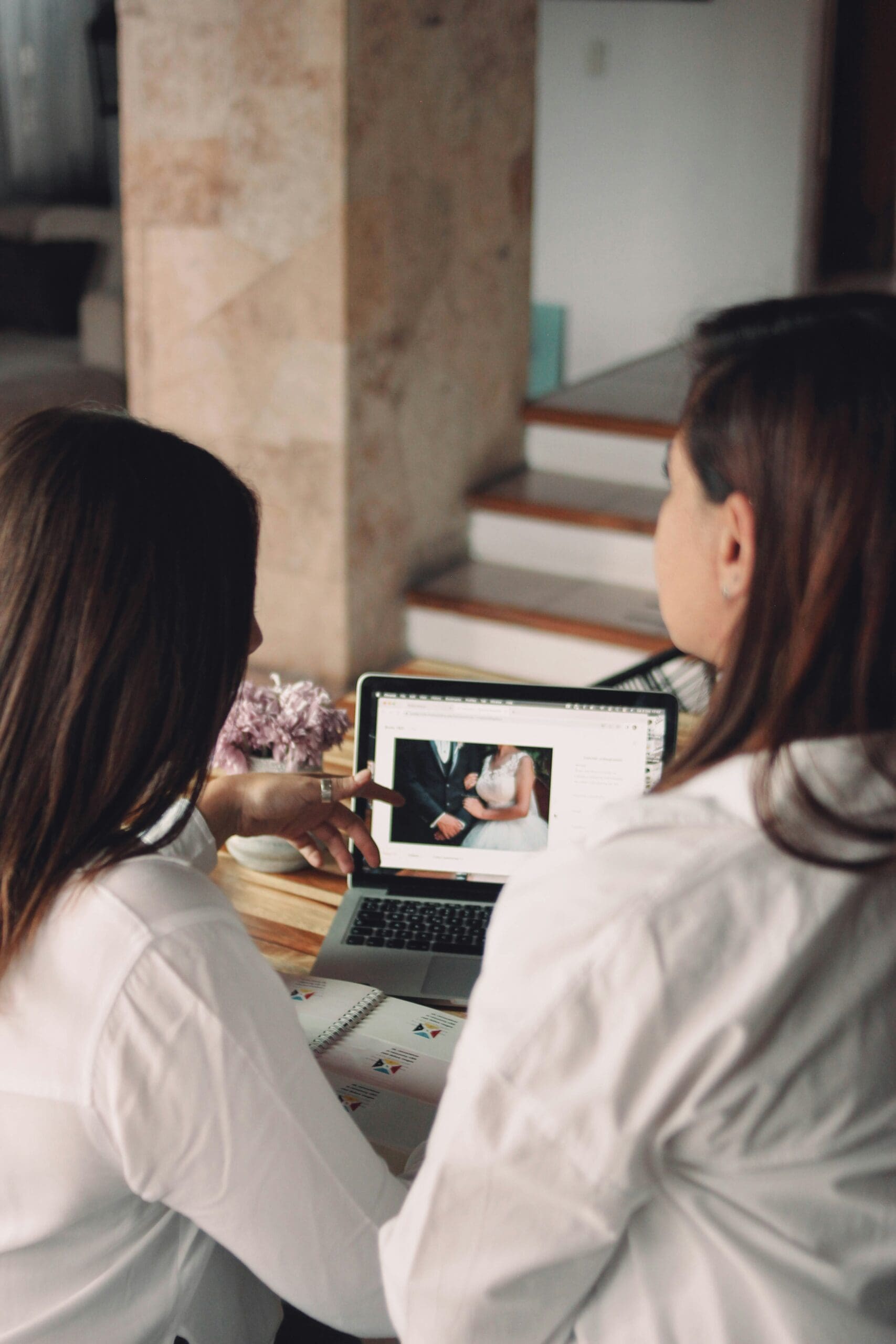 Two individuals looking at a laptop displaying a wedding image, representing the importance of visually showcasing expertise online to attract dream wedding clients. #weddingportfolio #onlinepresence #clientattraction