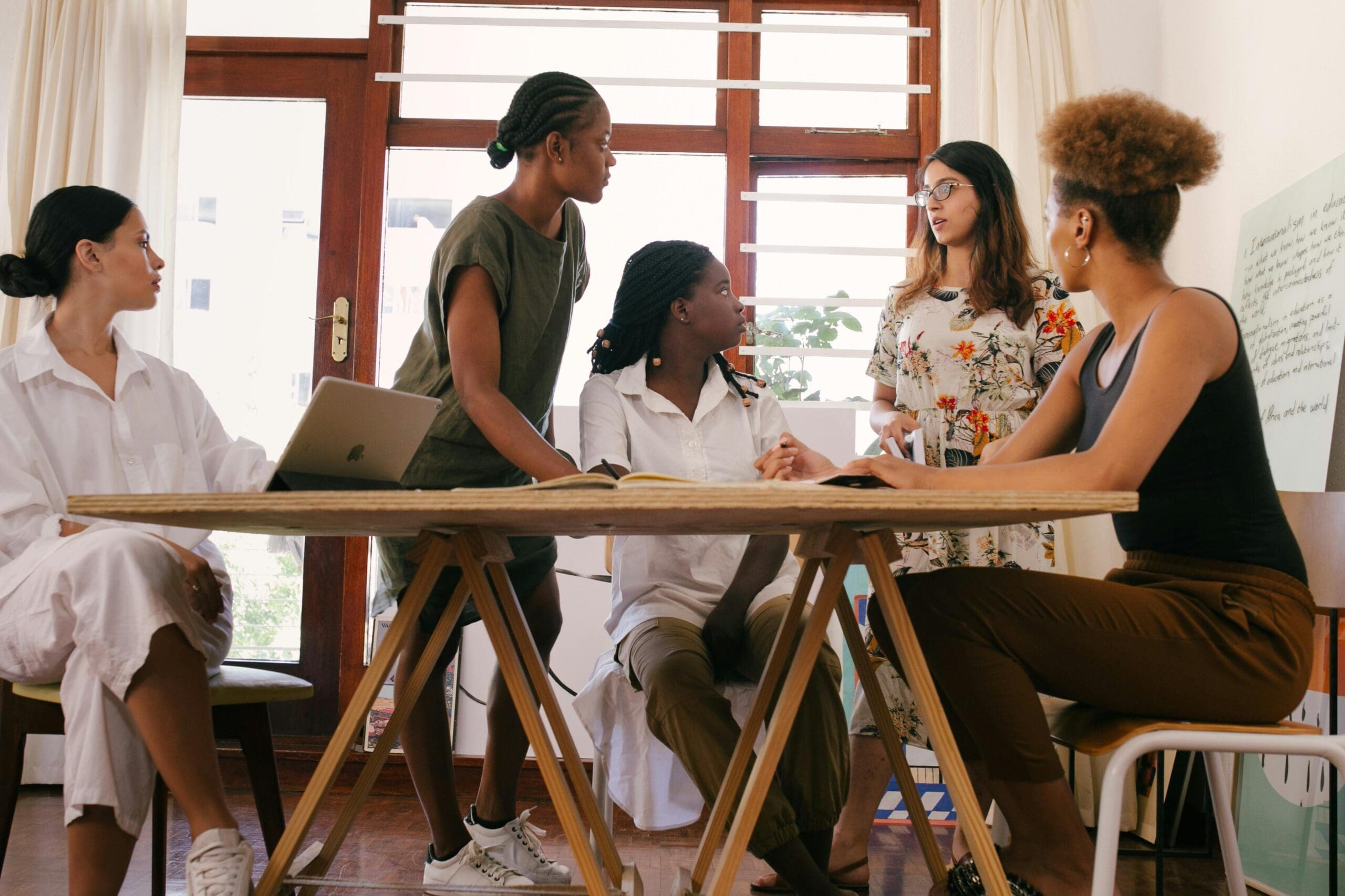 A group of women are gathered around a table, seemingly collaborating or discussing ideas, symbolizing the connection and community that a website for a women's collective should foster through its design. #womenscollective #communitywebsite #connection