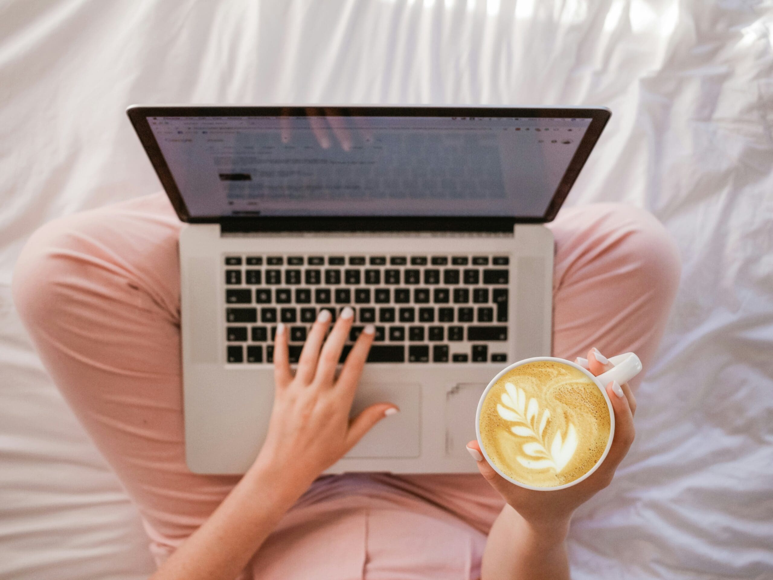 Overhead shot of someone working on a laptop with a latte, illustrating a visually appealing blogging workflow that aligns with a strong brand aesthetic. #brandbuilding #blogstrategy #aestheticworkflow